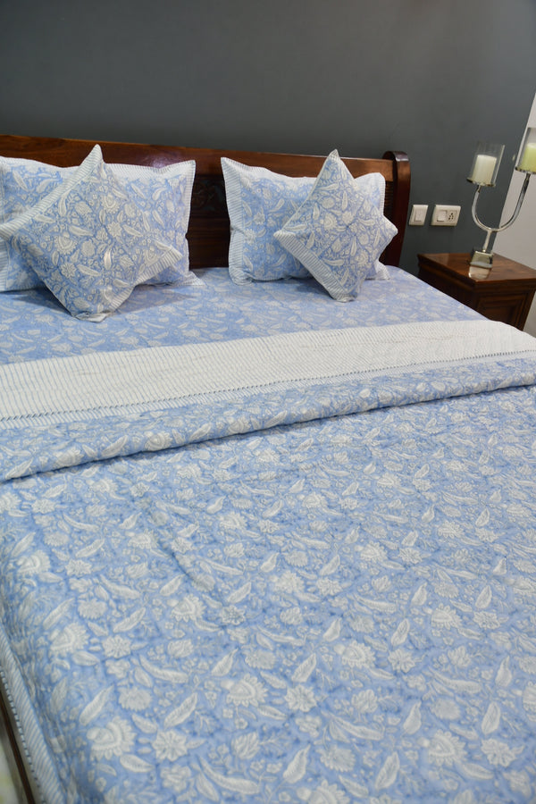 Bed with blue floral bedding and pillows against a gray wall.