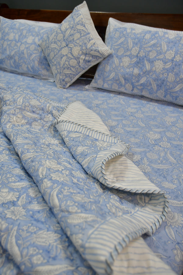 Blue and white patterned fabric with pillows and a blanket on a wooden surface