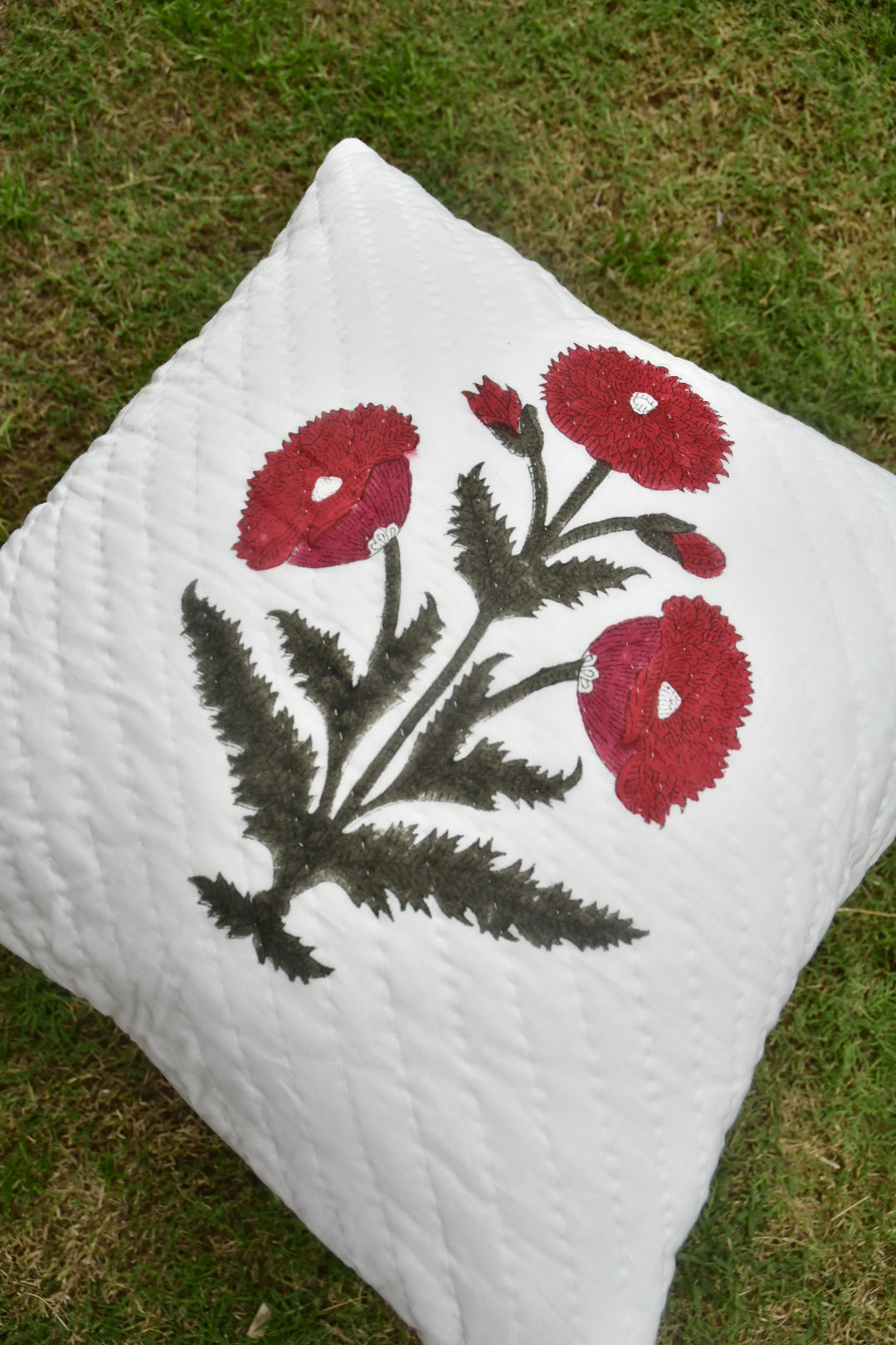 White pillow with red floral embroidery on a grassy background