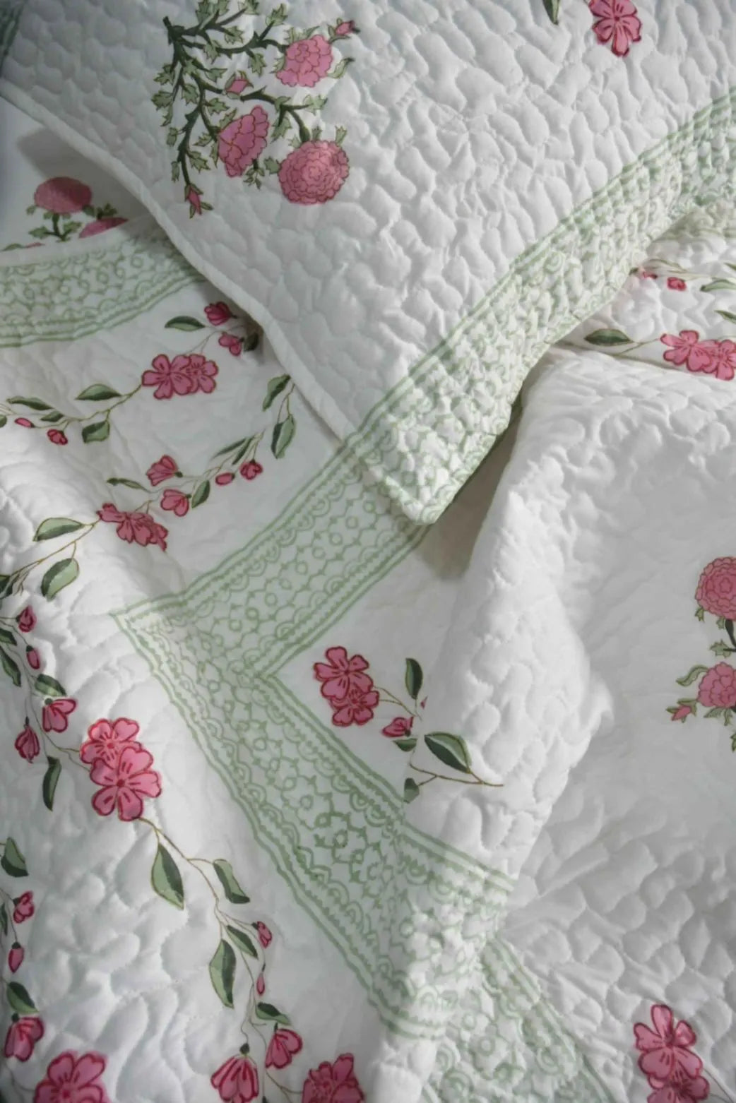 Floral quilt with pink flowers and green leaves on a white background