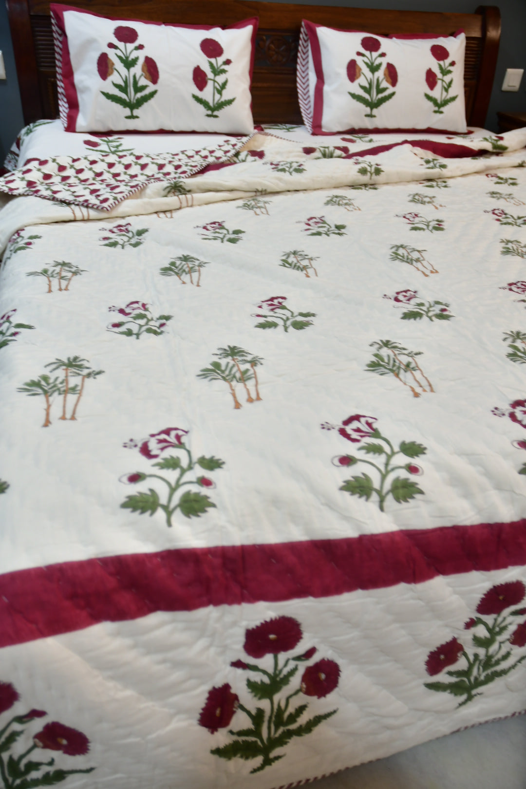 Floral patterned quilt with red and green details on a wooden bed frame.