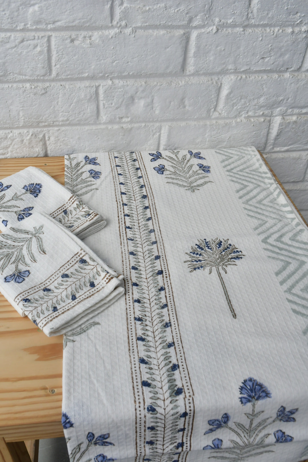 Embroidered tablecloth with floral patterns on a wooden surface against a white brick wall.