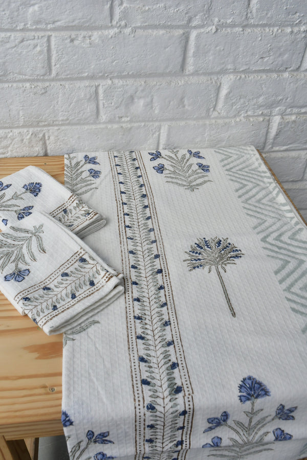 Embroidered tablecloth with floral patterns on a wooden surface against a white brick wall.