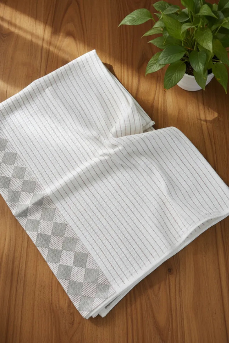Folded white towel with gray diamond pattern on a wooden surface with a plant in the background