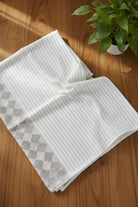 Folded white towel with gray diamond pattern on a wooden surface with a plant in the background