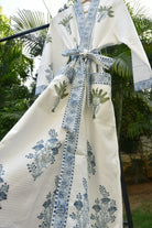 White garment with blue floral patterns and a large bow, hanging against a natural background.