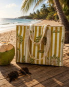 Striped beach bag with palm tree design on a wooden surface by the ocean.