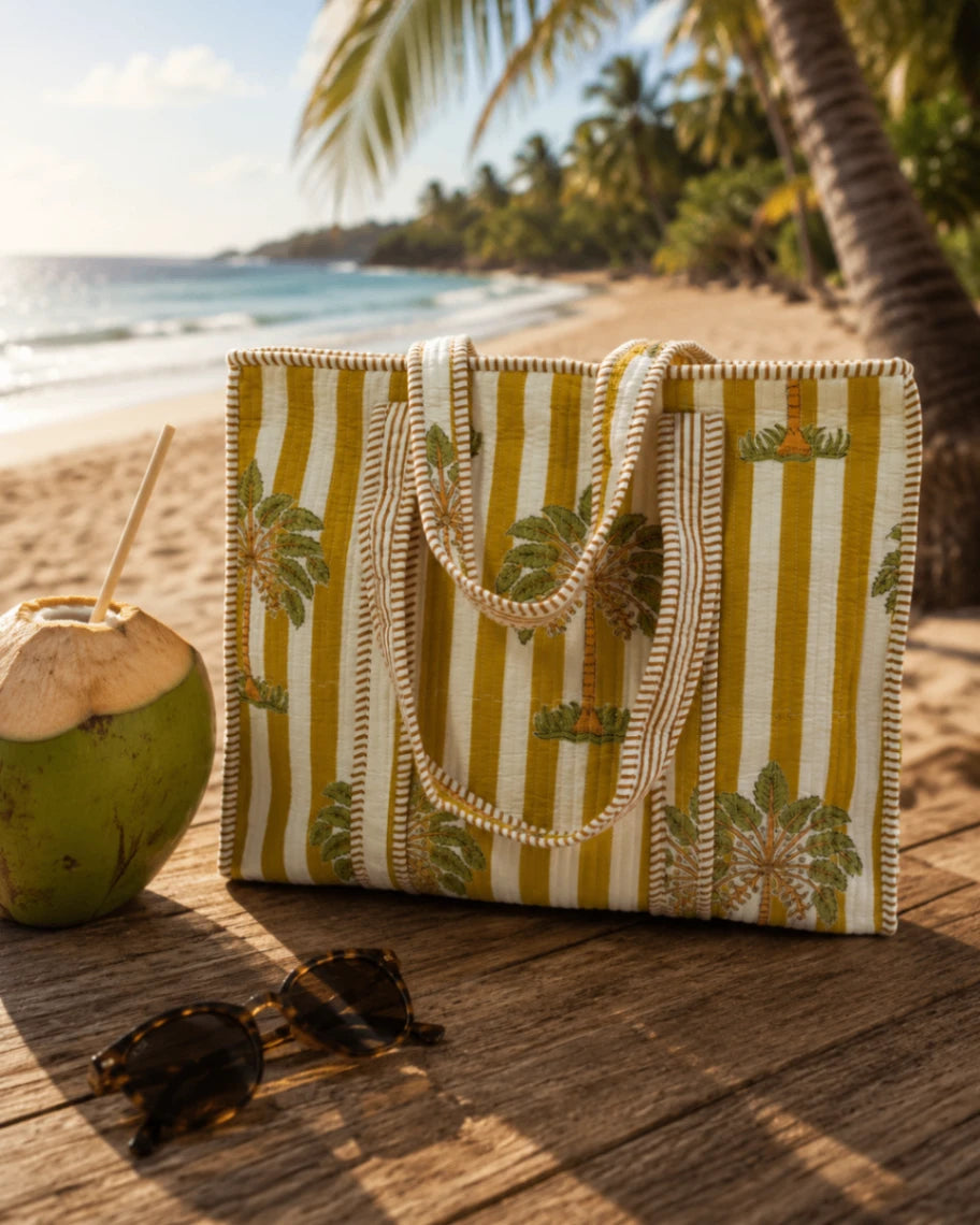 Striped beach bag with palm tree design on a wooden surface by the ocean.