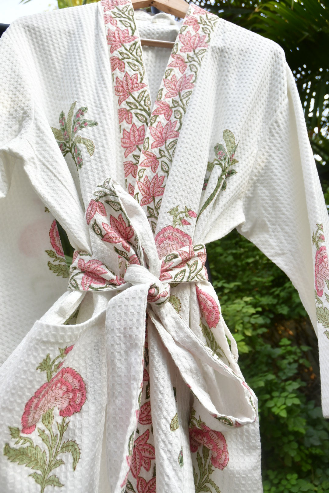 White bathrobe with pink floral patterns tied into a bow against a blurred green background