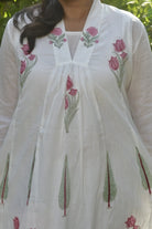 White embroidered dress with pink floral patterns on a blurred natural background