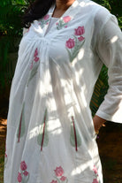 White embroidered dress with pink floral patterns worn by a person outdoors.