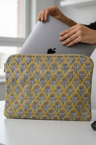 Person holding a laptop with a yellow and gray patterned sleeve on a white surface.