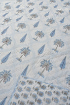 A close-up of a light blue and white quilted jaipuri design featuring embroidered palm trees and leaf motifs, with a braided border visible on the right.