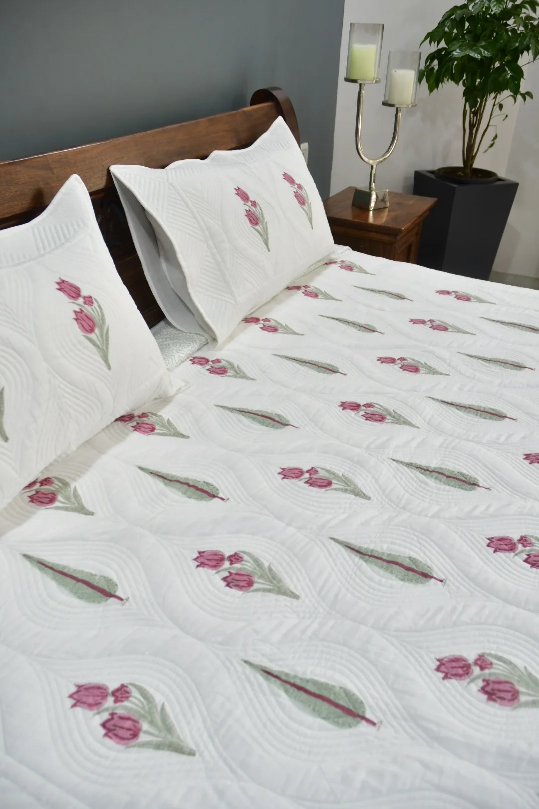 Floral patterned quilt on a bed with pillows and a nightstand in the background.