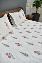 Floral patterned quilt on a bed with pillows and a nightstand in the background.