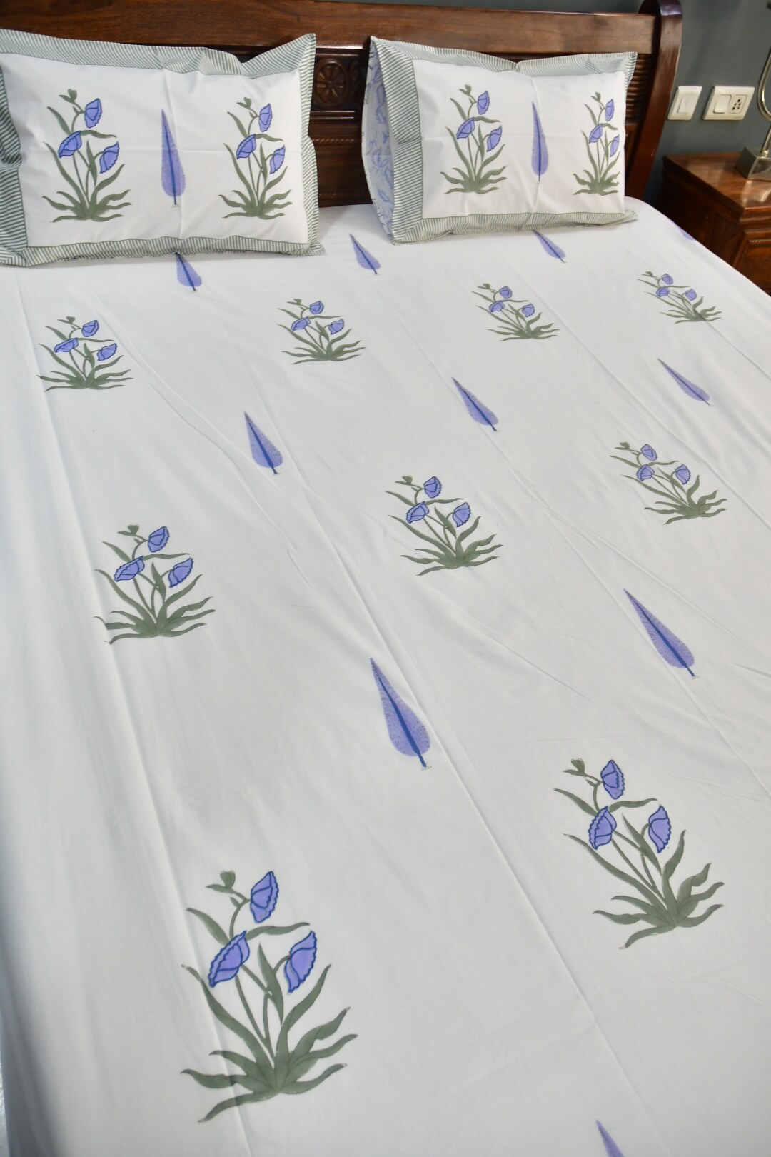 White bed sheet with a repeating pattern of blue iris flowers and green leaves, styled on a bed with matching pillowcases.