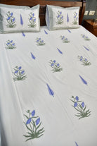 White bed sheet with a repeating pattern of blue iris flowers and green leaves, styled on a bed with matching pillowcases.