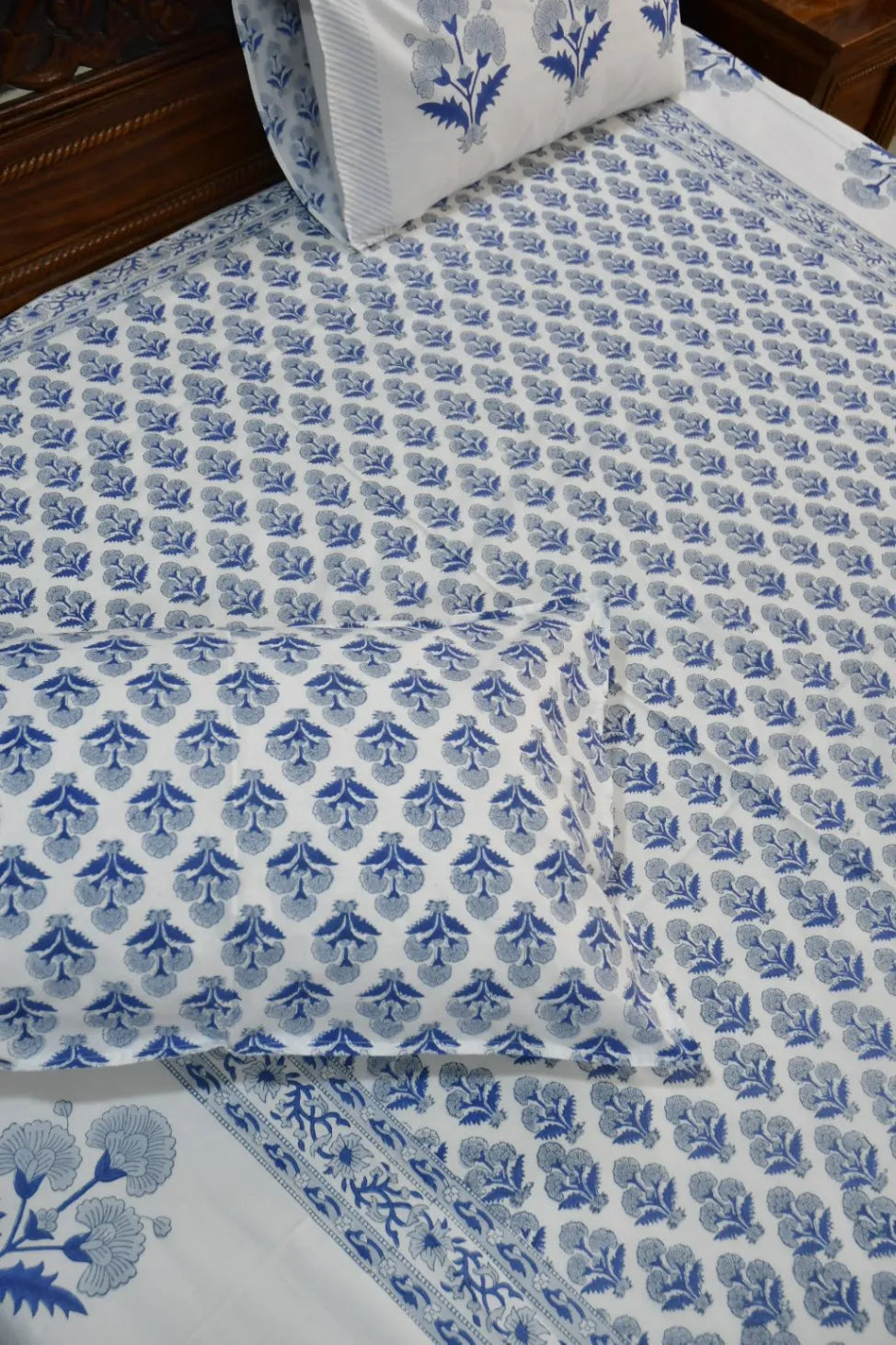 Blue floral patterned bedspread on a bed with matching pillows.