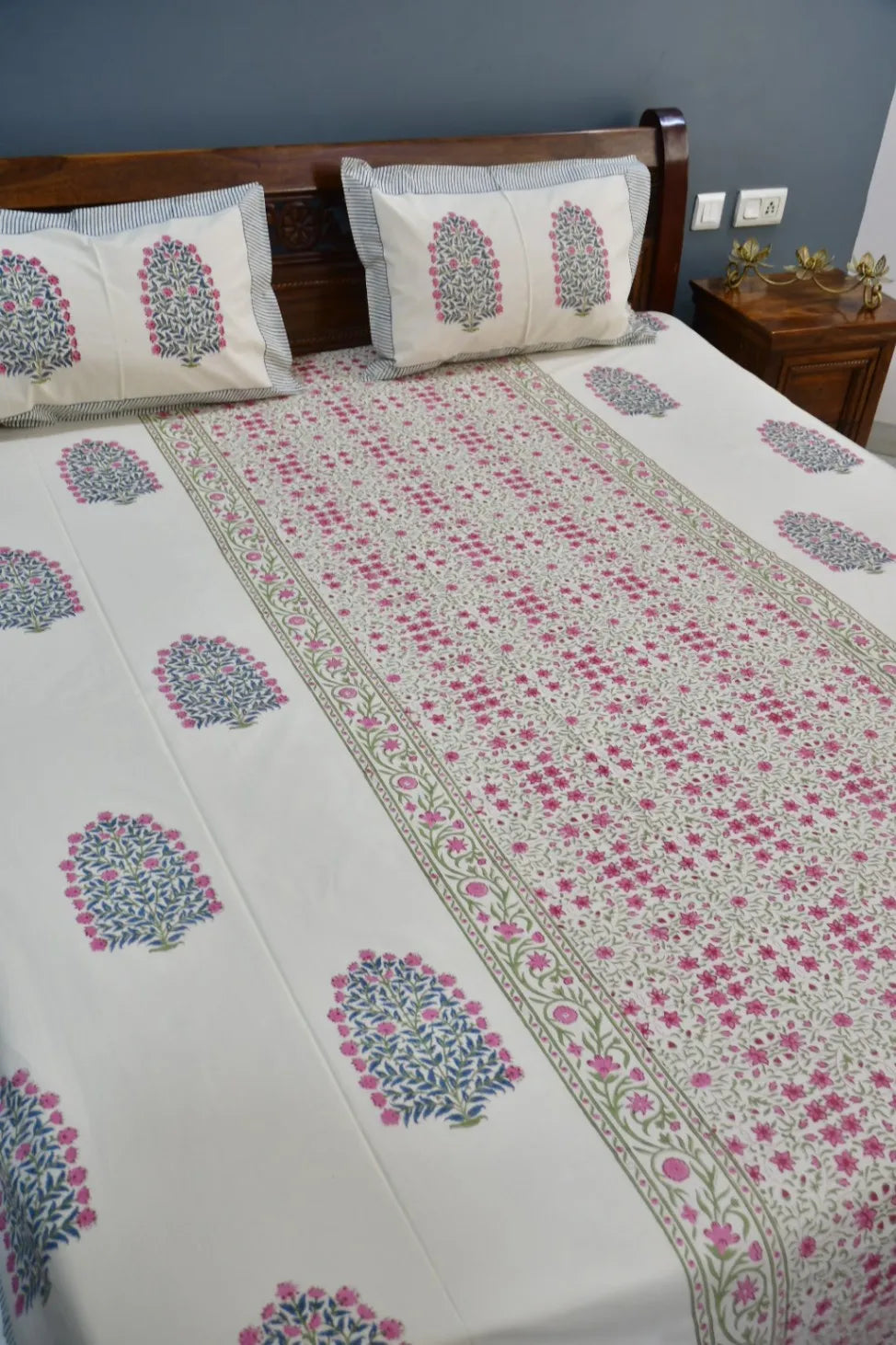 Bed with floral patterned bedspread and pillows in a bedroom setting.