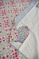 A close-up of a white dohar with a dense pink floral print, a blue and white striped border, and a central embroidered floral motif in pink, green, and blue.