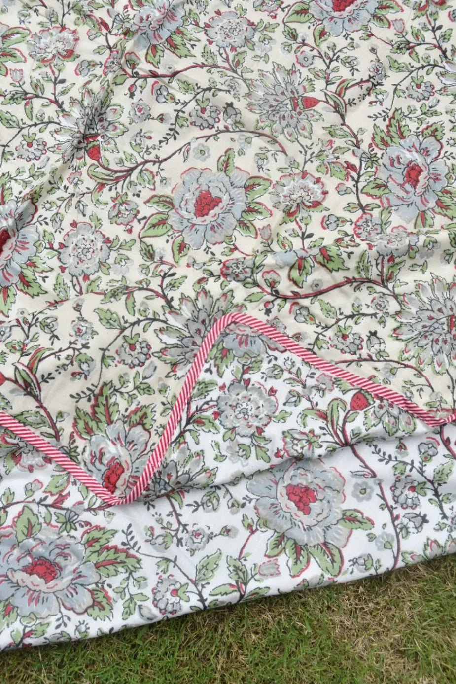 Floral patterned AC comforter with red and green accents on a grassy background