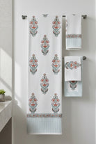 A set of white waffle-weave towels with a teal and rust orange botanical damask pattern, hanging on a silver metal towel bar against a white wall.