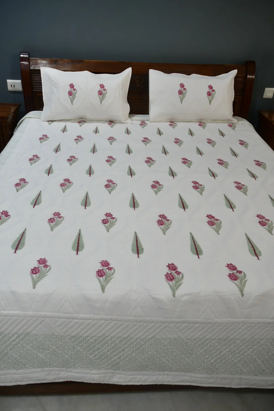 Floral patterned bedspread on a wooden bed with white pillows.