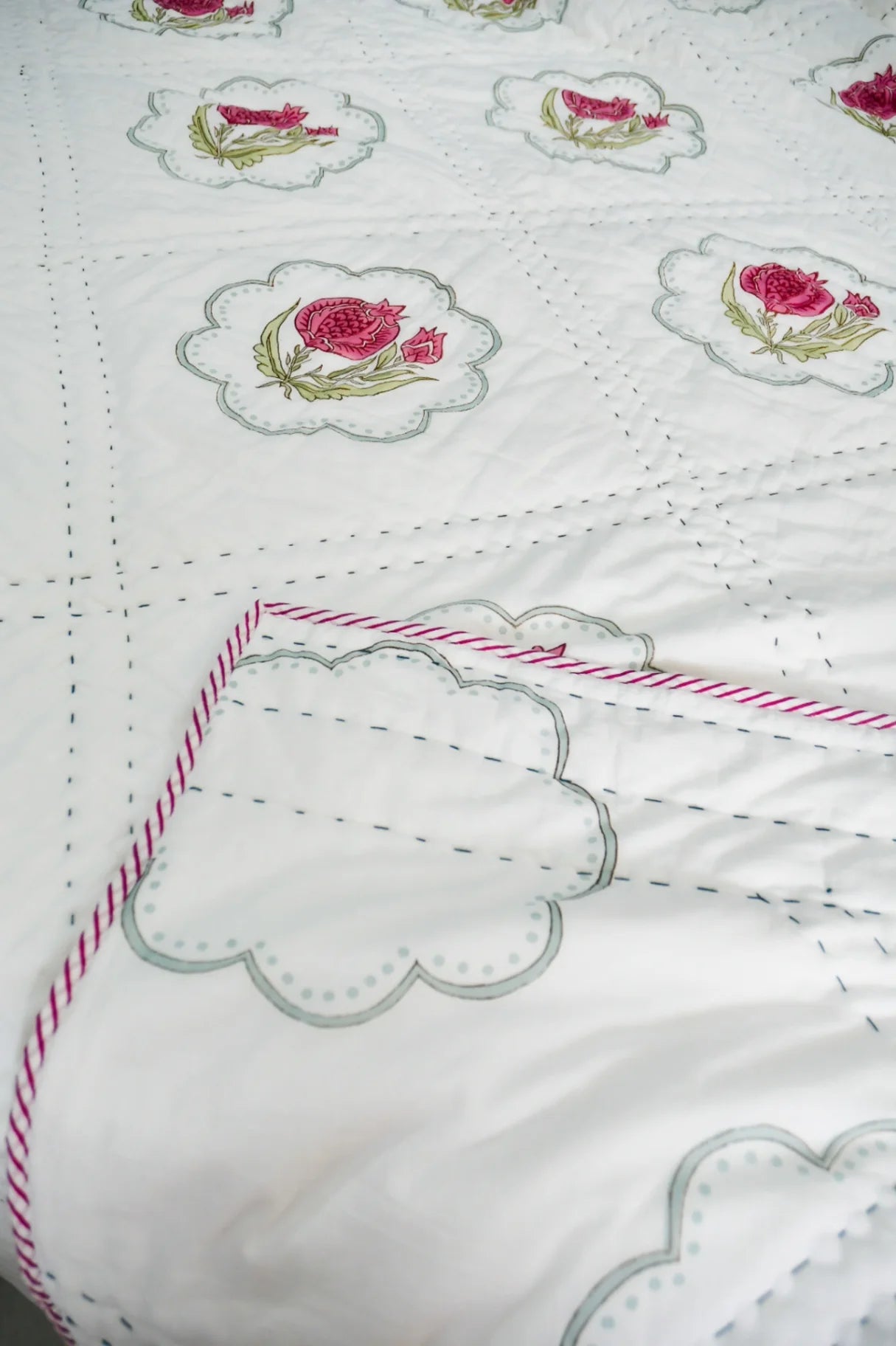 Close-up of a white fabric with embroidered pink roses and green leaves.