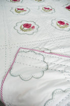 Close-up of a white fabric with embroidered pink roses and green leaves.