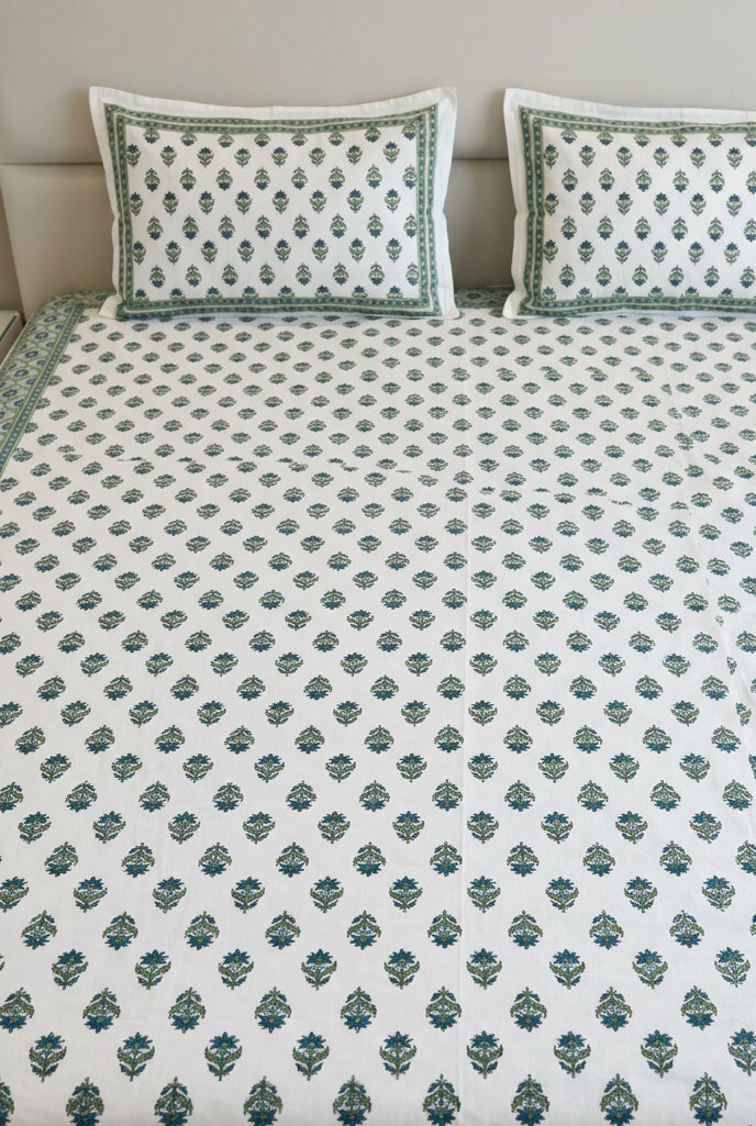 A white cotton bedspread set with a green block print pattern and matching pillowcases, displayed on a bed in a bedroom setting.