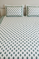 A white cotton bedspread set with a green block print pattern and matching pillowcases, displayed on a bed in a bedroom setting.