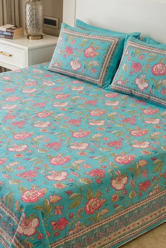 A turquoise blue floral bedspread set with matching pillowcases, featuring pink and red roses with green leaves and ornate borders, styled on a bed in a bedroom setting.