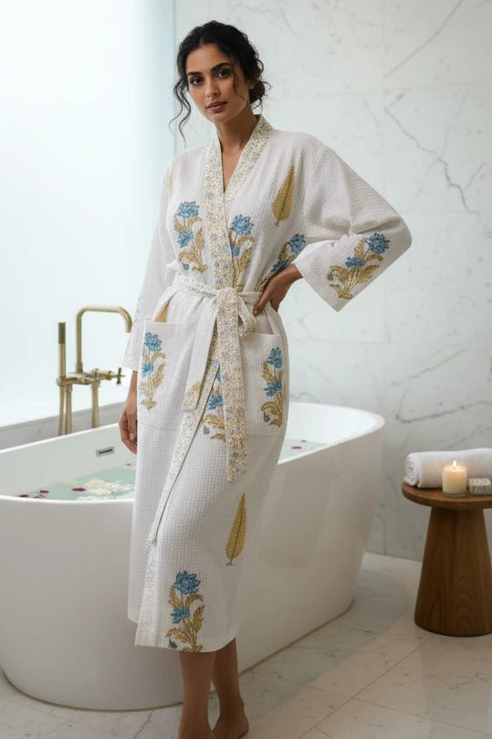 A woman wearing a white waffle-knit bathrobe with blue and gold floral embroidery, standing in a modern bathroom next to a freestanding bathtub.