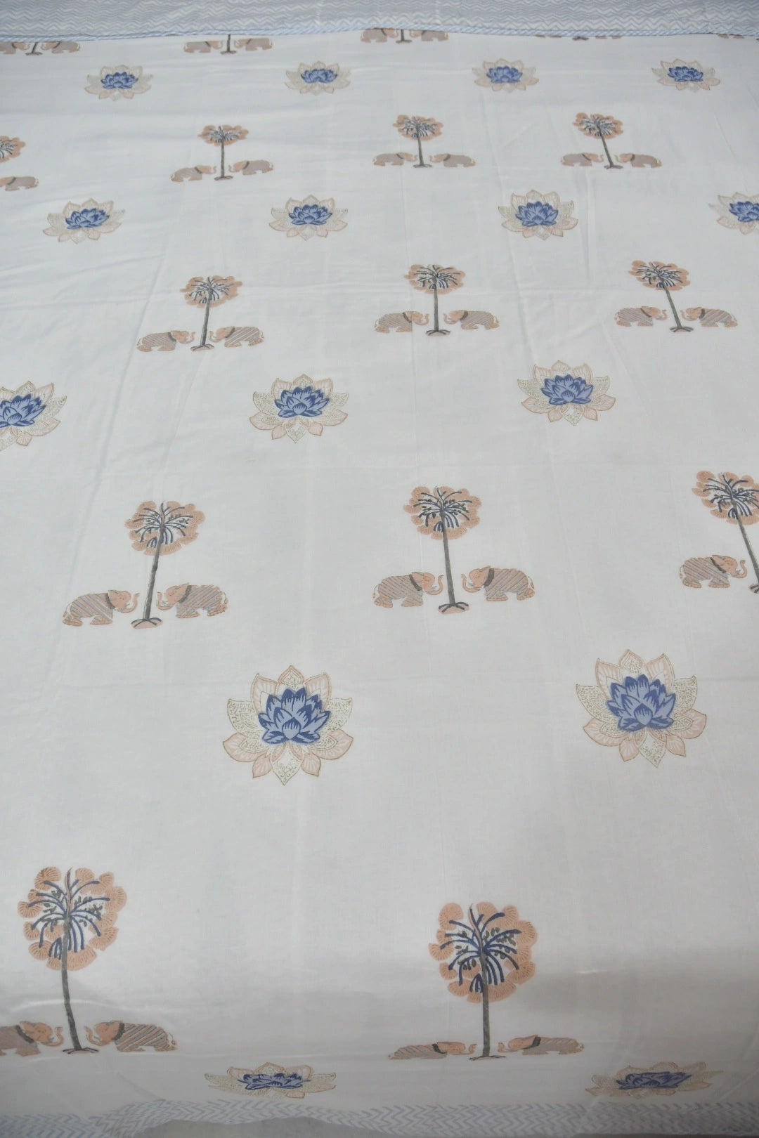White cotton dohar printed with a repeating pattern of lotus flowers in blue and beige palm trees.
