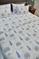 A light blue and white quilted Bedding Set with a repeating palm tree pattern, styled on a bed with matching decorative pillows in a bedroom setting.