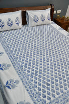 Bed with blue floral patterned bedding and pillows against a gray wall.