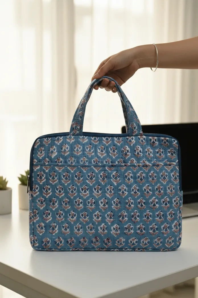 Blue patterned laptop bag held by a hand on a white surface with a blurred background