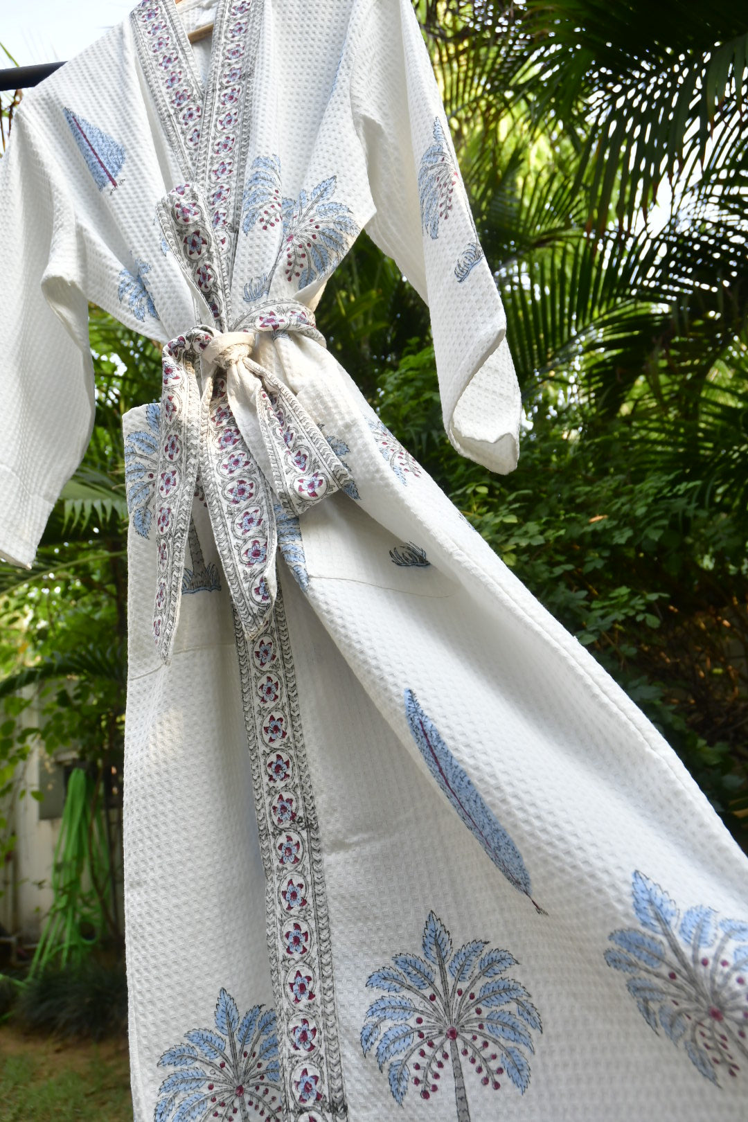 Close-up of a white robe with blue floral patterns and decorative trim against a blurred green background.