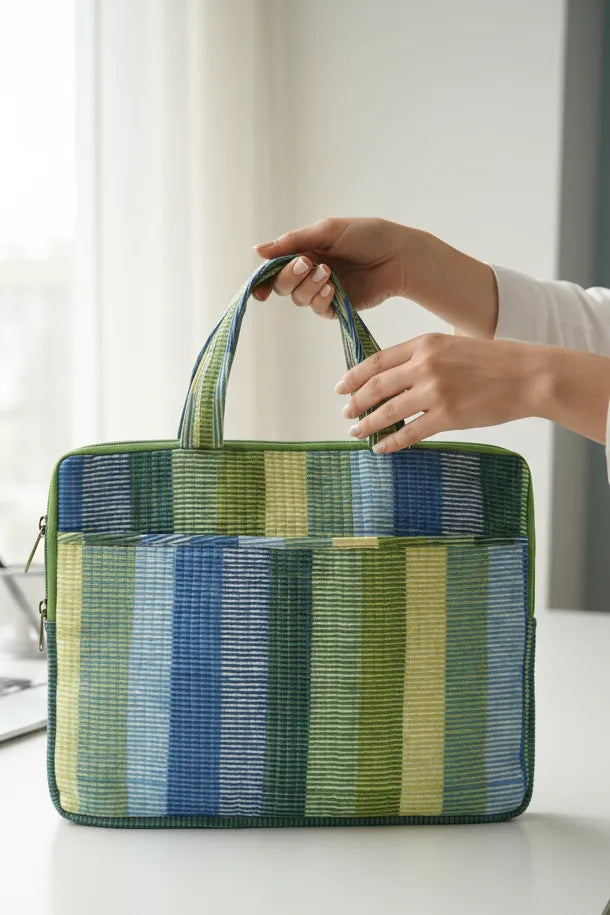 Hand holding a striped green and blue bag on a white surface
