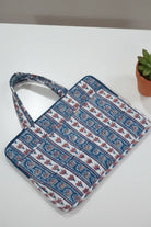 Blue and white patterned bag on a white surface with a small plant in the background