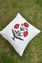 White pillow with red floral embroidery on a grassy background