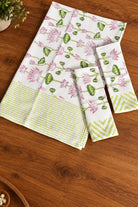 A set of three white cotton kitchen towels with pink lotus floral prints and green borders, arranged on a wooden tabletop.