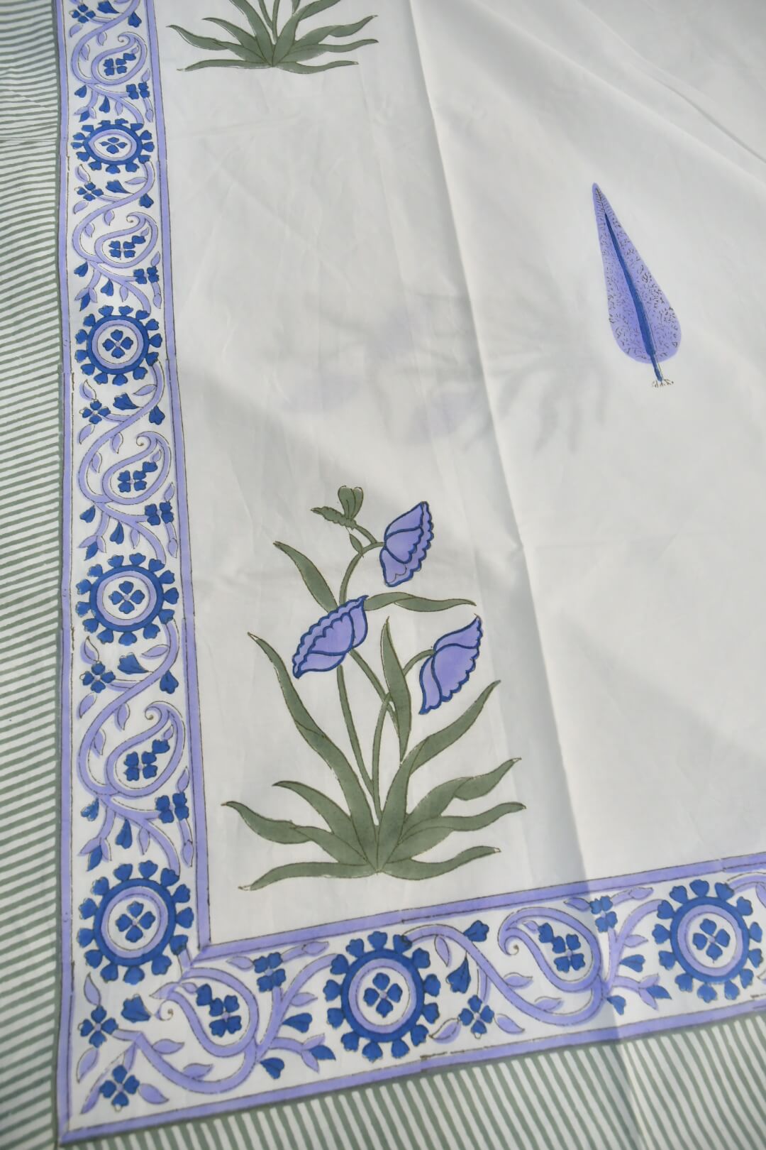 A close-up of a bedsheet featuring a decorative border with blue and purple floral motifs and a central floral print in blue and green.