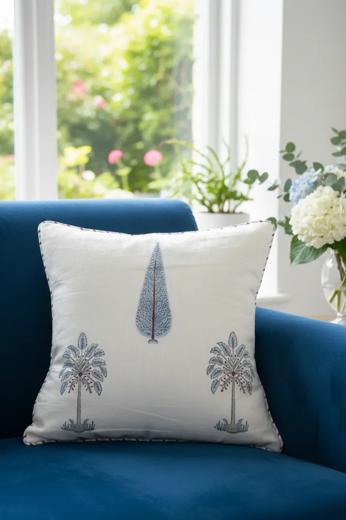 Decorative cushion cover with tree patterns on a blue couch in a bright room with flowers & plants.