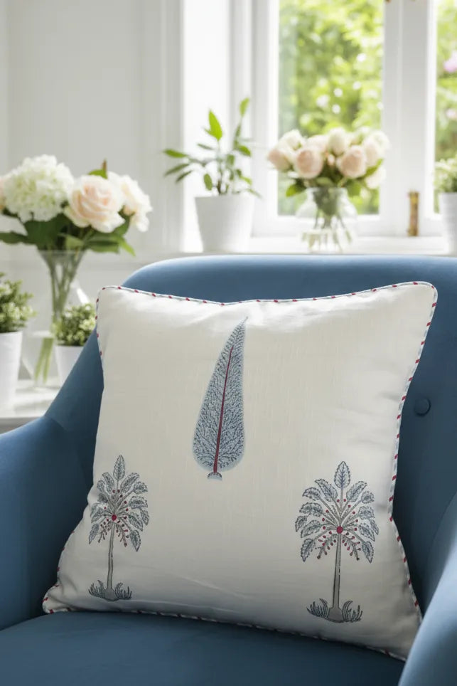 Decorative cushion cover with tree patterns on a blue chair in a bright room with flowers and plants.