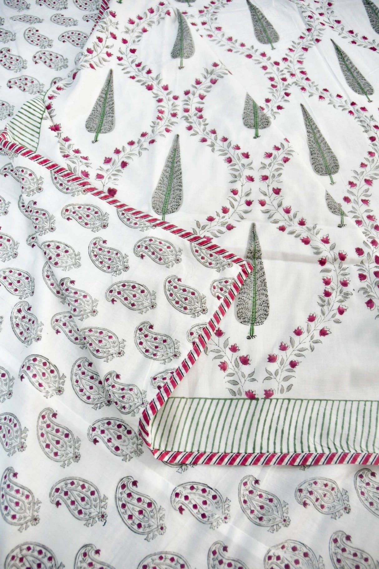 A close-up of a white dohar with printed paisley and tree motifs in gray and pink, plus a striped border with red and green accents.