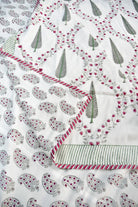 A close-up of a white dohar with printed paisley and tree motifs in gray and pink, plus a striped border with red and green accents.