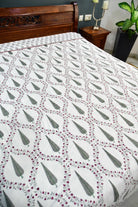 A white dohar with a repeating green and burgundy floral pattern, styled on a bed in a bedroom setting.
