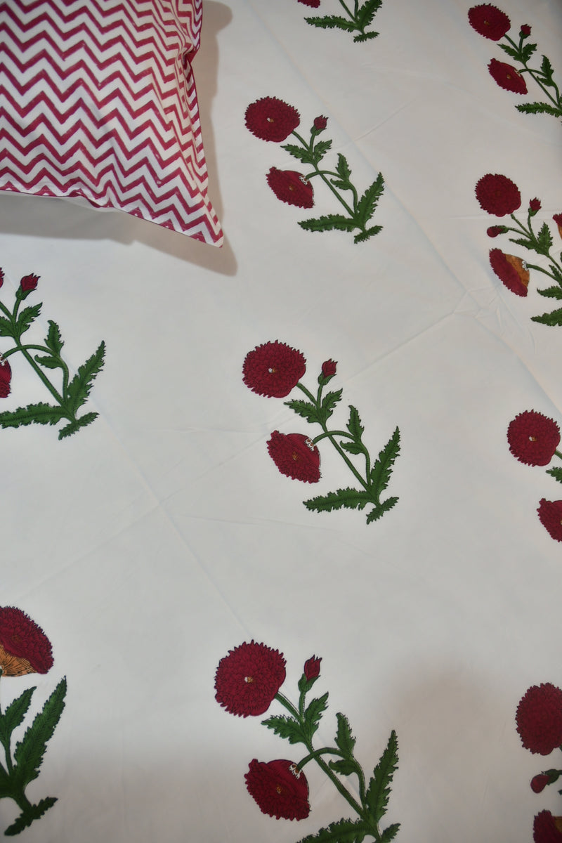 Floral patterned fabric with red flowers and green leaves on a white background, with a red and white zigzag pillow partially visible.