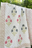 Floral patterned quilt with pink and green flowers on a white background, outdoors.